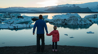 Parent and child holding hands looking at icebergs in the horizon